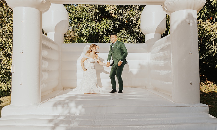 bride and groom jumping in white bouncy house 