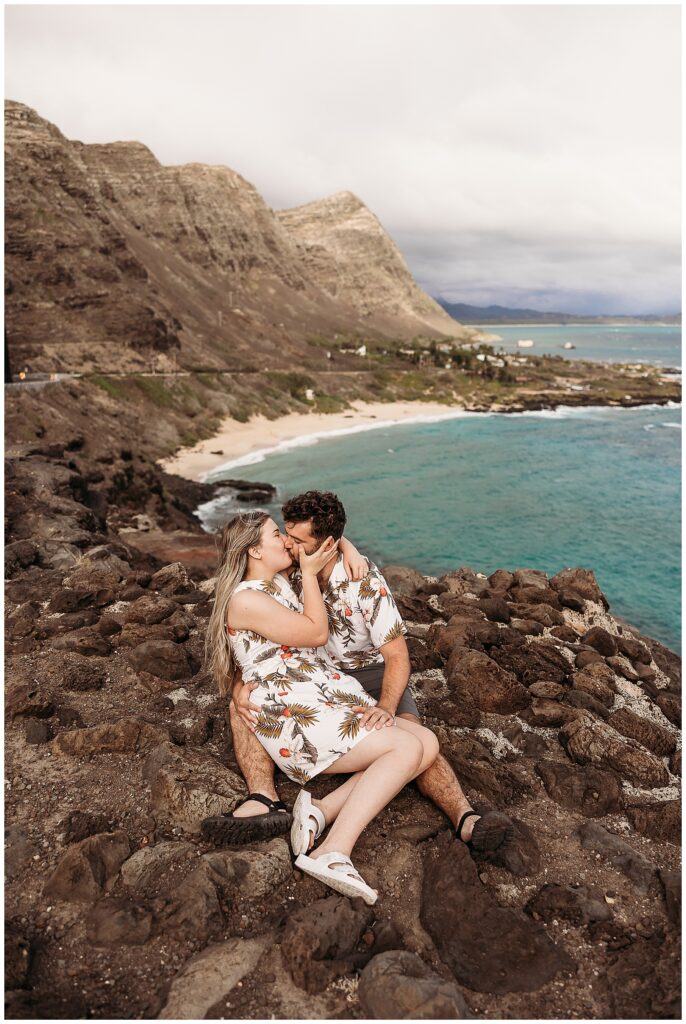 Couple sitting on lava rocks on a cliff overlooking makapuu beach