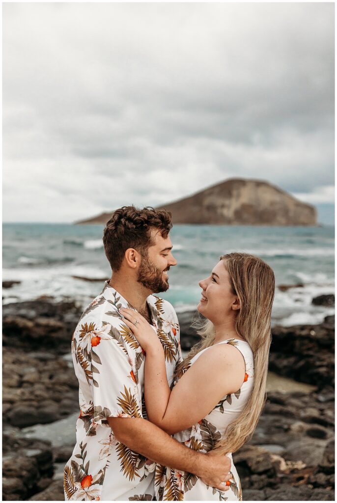 Couple looking at each other smiling with ocean in background